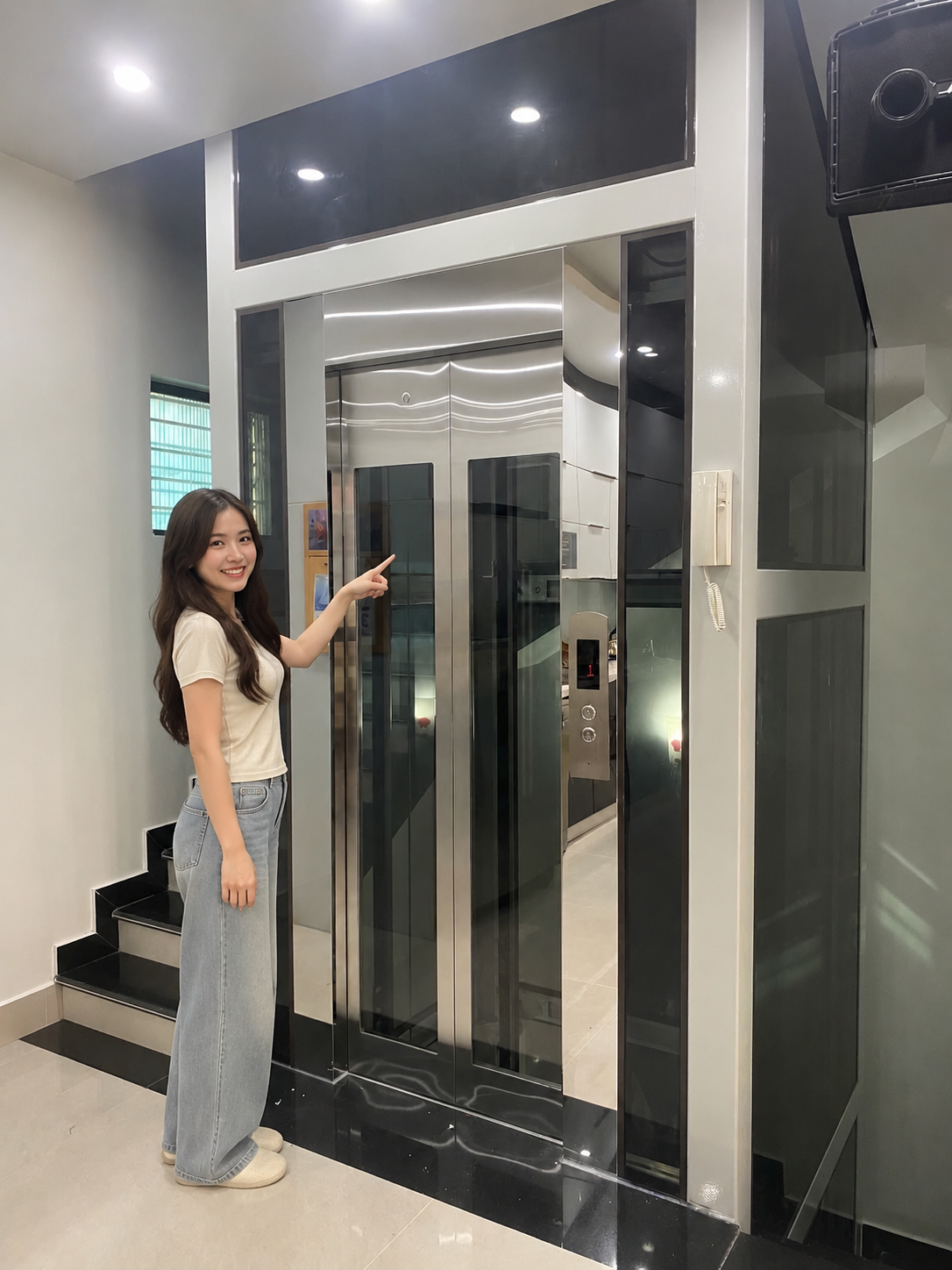 Cô gái đứng cạnh và chỉ tay vào thang máy gia đình cửa kính khung inox trong nhà